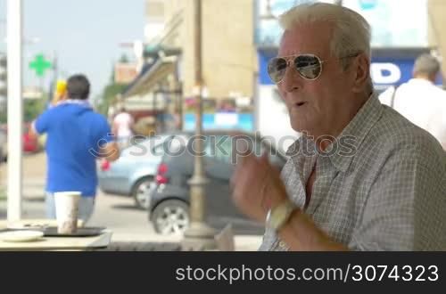 Close-up of senior man wearing aviator sunglasses and smoking cigarette while sitting in cafe in summer.