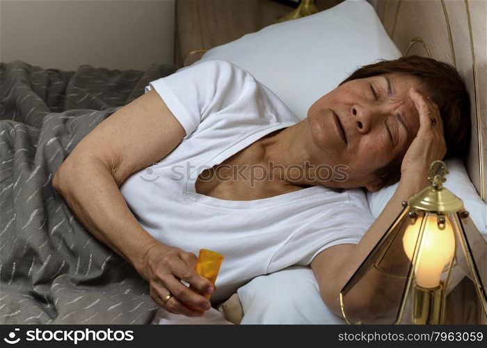 Close up of senior woman, eyes open while touching forehead, holding medicine container. Insomnia concept.