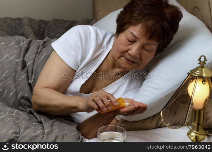 Close up of senior woman, taking medicine out of bottle, while in bed. Sick concept.