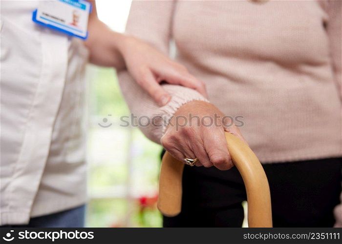 Close Up Of Senior Woman With Hands On Walking Stick Being Helped By Care Worker