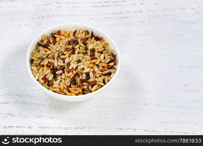 Close up of several whole grains of rice in bowl on white wood.