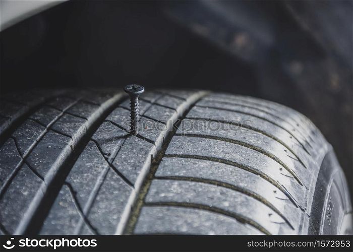 Close up of sharp metal screw puncturing into a car tire