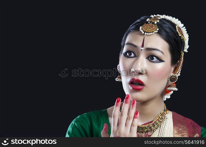 Close-up of shocked Bharatanatyam dancer performing on black background