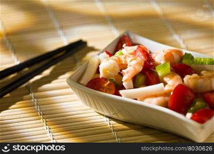 Close up of shrimp salad with squid tomatoes celery inside a white bowl over a bamboo tablecloth and chopsticks. Close up of shrimp salad over a bamboo tablecloth and chopsticks