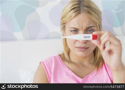 Close-up of sick woman taking temperature with thermometer in bed