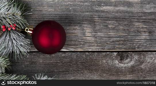 Close up of single red ball ornament with frost snow fir branches and wooden background for a merry Christmas or happy New Year celebration concept
