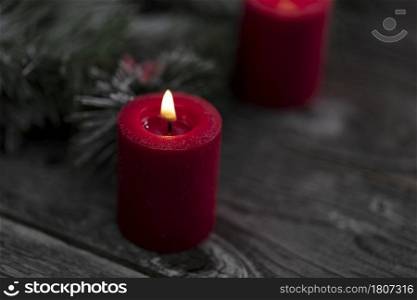 Close up of single red glowing candle with fir branches and wooden dark background for a merry Christmas or happy New Year celebration concept