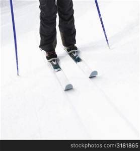 Close up of skier legs boots poles and skis standing on slope.