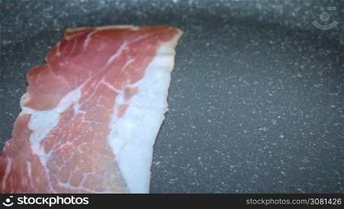 Close up of slices of bacon lays on the hot grill being fried. Slow motion footage.