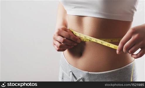 Close up of slim woman measuring her waist&rsquo;s size with tape measure. Isolated on white background.. Close up of slim woman measuring her waist&rsquo;s size with tape measure.