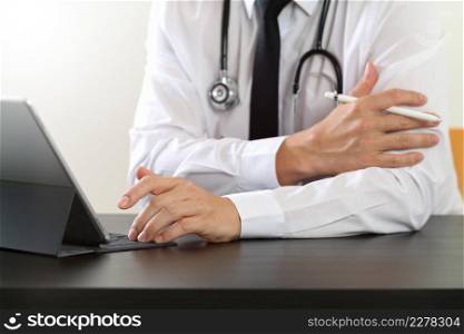 close up of smart medical doctor working with digital tablet computer and stylus pen and stethoscope on dark wooden desk