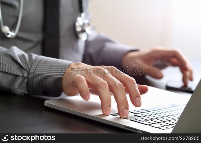 close up of smart medical doctor working with laptop computer and mobile phone and stethoscope on dark wooden desk