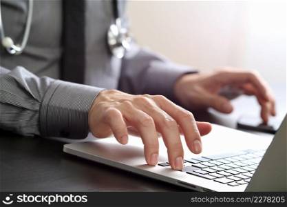 close up of smart medical doctor working with laptop computer and mobile phone and stethoscope on dark wooden desk