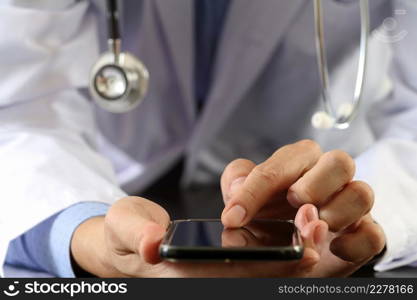 close up of smart medical doctor working with smart phone and stethoscope on dark wooden desk with glass reflected view
