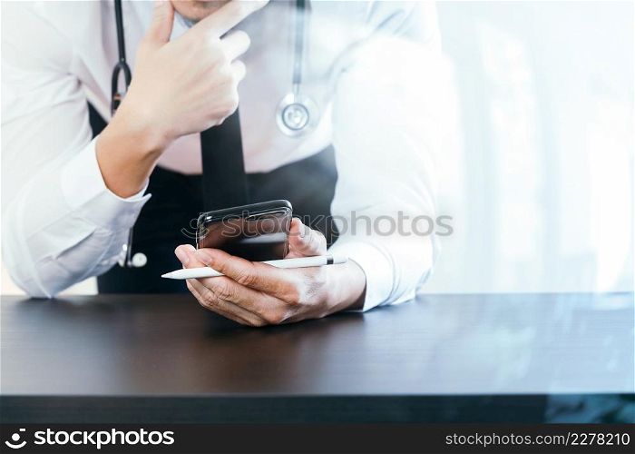 close up of smart medical doctor working with smart phone and stethoscope on dark wooden desk with glass reflected view