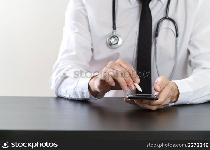 close up of smart medical doctor working with smart phone and stethoscope on dark wooden desk