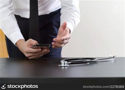 close up of smart medical doctor working with smart phone and stethoscope on dark wooden desk