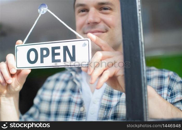Close Up Of Smiling Male Small Business Owner Turning Around Open Sign On Shop Or Store Window Or Door
