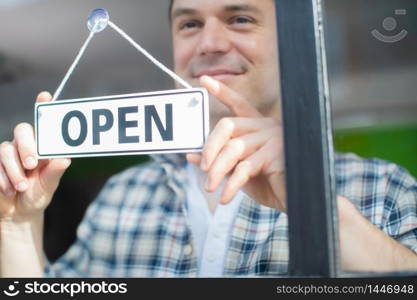 Close Up Of Smiling Male Small Business Owner Turning Around Open Sign On Shop Or Store Window Or Door