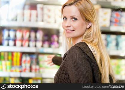 Close-up of smiling woman reaching for products arranged in refrigerator and looking at camera