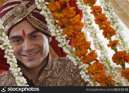 Close-up of smiling young Indian bridegroom behind wreath