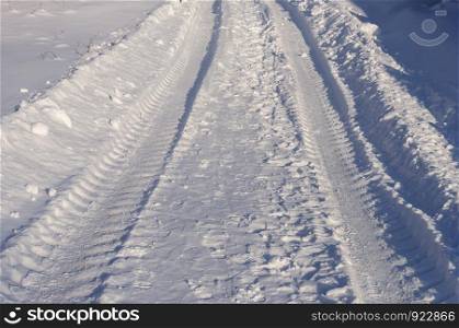 Close-up of snowy country road, tire track, sunny winter day