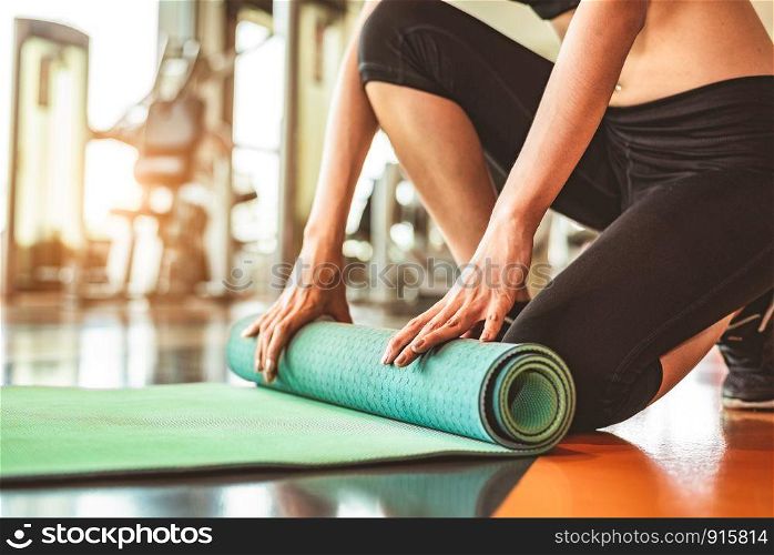 Close up of sporty woman folding yoga mattress in sport fitness gym training center background. Exercise mat rolling keeping after yoga class. Workout and sport training concept. Hands on carpet