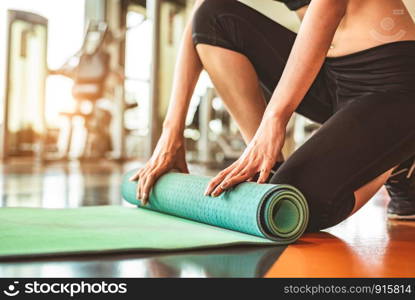 Close up of sporty woman folding yoga mattress in sport fitness gym training center background. Exercise mat rolling keeping after yoga class. Workout and sport training concept. Hands on carpet