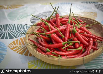 Close-up of stacked fresh red peppers with stems on a bamboo basket.
