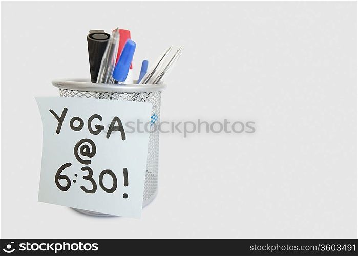 Close-up of sticky note with yoga message on pen holder over white background