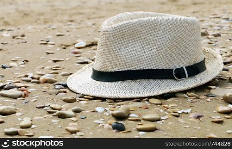Close up of straw hat on a sandy and grey stone beach. Summer time vacation. Concept of travel background. Flat lay and copy space.. Close up of straw hat on a sandy and grey stone beach. Summer time vacation. Concept of travel background.