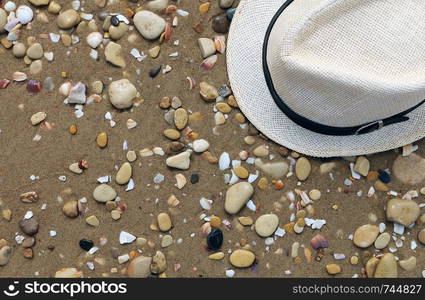 Close up of straw hat on a sandy and grey stone beach. Summer time vacation. Concept of travel background. Flat lay and copy space.. Close up of straw hat on a sandy and grey stone beach. Summer time vacation. Concept of travel background.