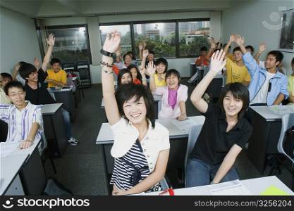 Close-up of students sitting in a classroom and raising their hands