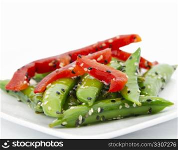 Close up of sugar snap pea salad garnished with sliced red pepper and sesame seeds