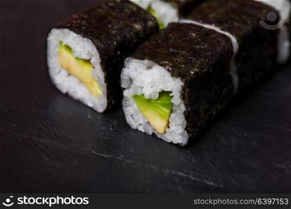Close-up of sushi rolls with avocado on a black slate background. Maguro sushi with tuna