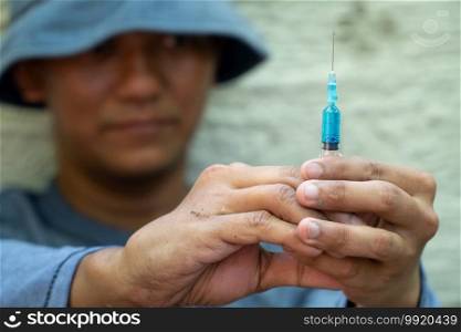close up of Syringe and Needle in hand of drug addict man. homeless using needle injecting liquid. Drug concept and Danger of drugs