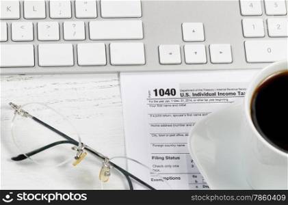 Close up of tax form, reading glasses, computer keyboard and coffee on white desk. Focus on Tax form 1040.