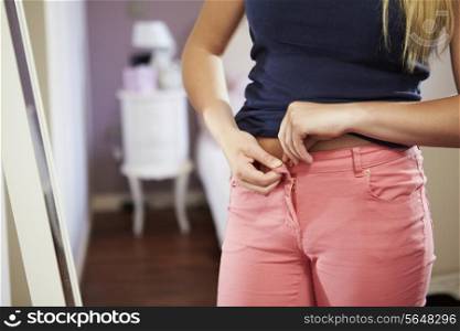 Close Up Of Teenage Girl Fastening Trousers In Bedroom