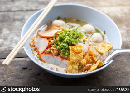 Close-up of Thai Noodle Soup with Meat in white bowl on wooden background.