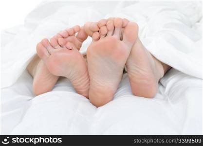 Close-up of the feet of a couple on the bed. Isolated on white background