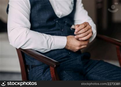 Close-up of the grooms male hands before the wedding.. A man is sitting in a wooden chair nervously fiddling with his shirt 3799.
