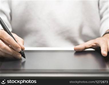 Close up of the hand of a graphic designer holding an electronic stylus. Background with free space for text, horizontal image . Graphic Designer Using Tablet and Stylus