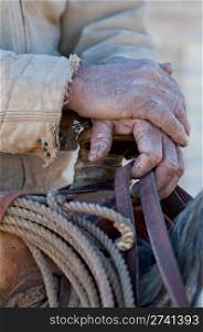 Close up of the hands of an old cowboy on his horse holding onto a saddle.