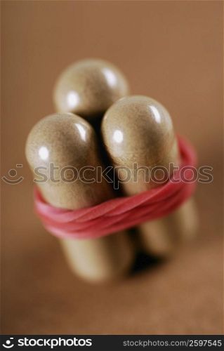 Close-up of three capsules tied with a rubber band