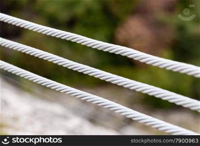Close-up of three parallel metal cables on blurred background.