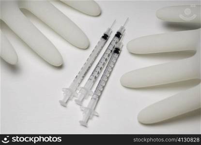 Close-up of three syringes with two gloves