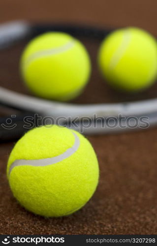 Close-up of three tennis balls and a racket in a court