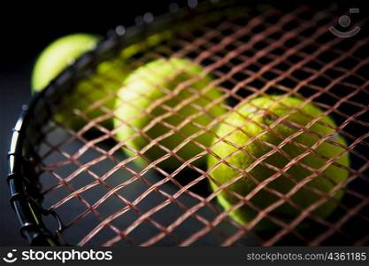 Close-up of three tennis balls with a tennis racket