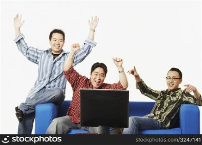 Close-up of three young men cheering in front of a flat screen monitor