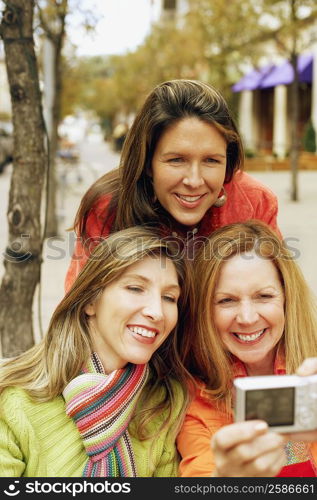 Close-up of three young women looking at a digital camera and smiling